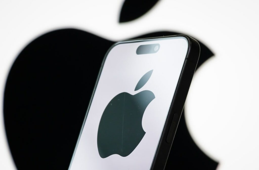 In this photo illustration, the logo of Apple Inc. is displayed on a smartphone screen, with the company's iconic black apple symbol visible in the background.