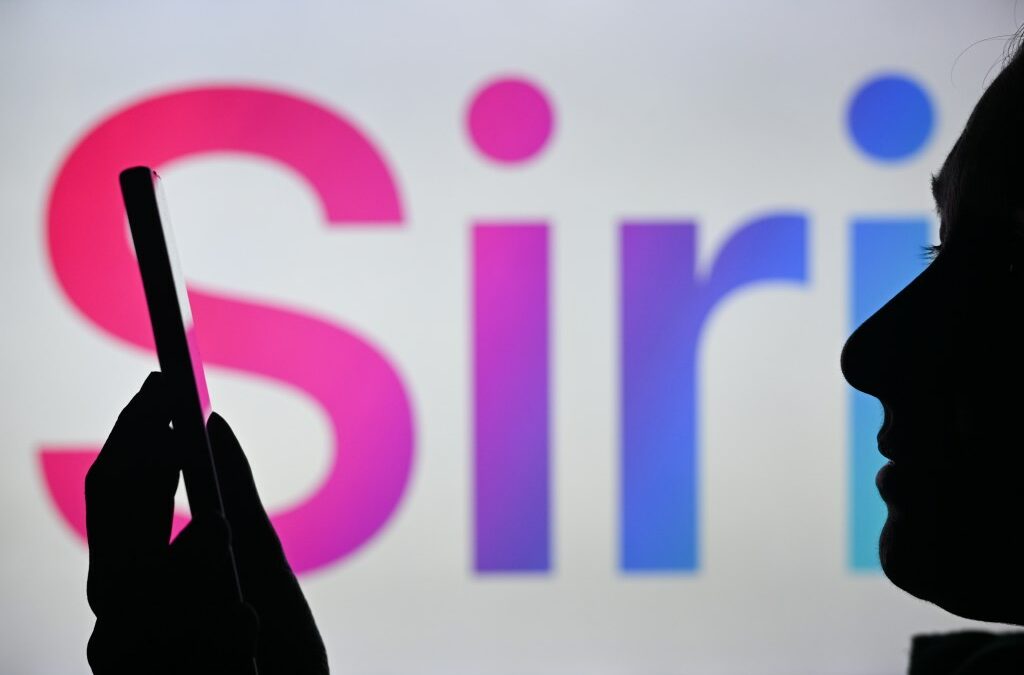 An image of a woman holding a cell phone in front of the Siri logo displayed on a computer screen.