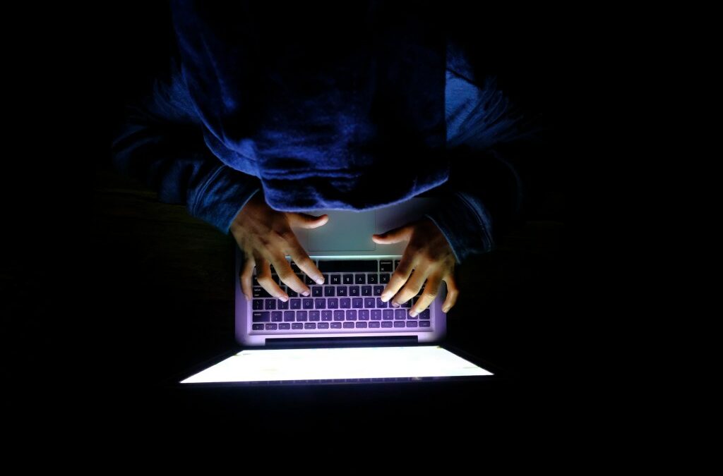 Hooded hacker Man with laptop stealing personal data from internet