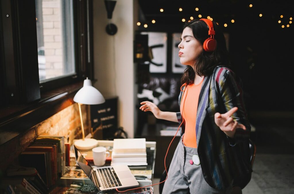 Young Latinx woman sitting at the desk in her Los Angeles apartment, receiving happy news over the social networks or just having a nice day, dancing to the music.