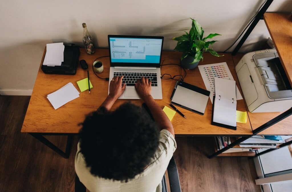 Overhead view of a woman working on a laptop while sitting at a cluttered desk