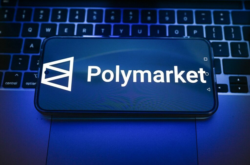 In this photo illustration, a Polymarket logo is displayed on a smartphone on top of a laptop.