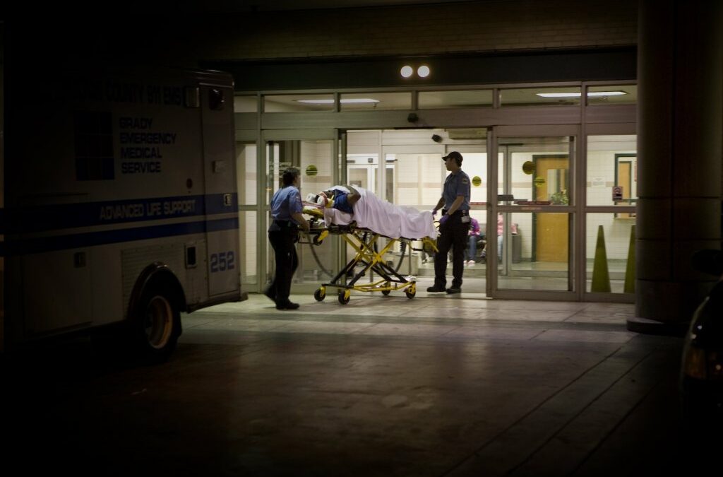 a person wheeled in on an ambulance stretcher outside of a U.S. emergency room at night
