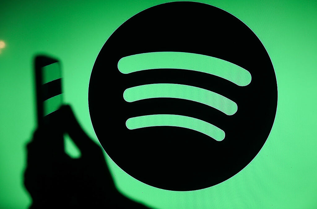 The Spotify logo displays on a screen with a person holding a phone.