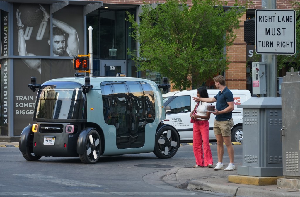 Pedestrians watch as a Zoox robotaxi passes along East Fifth Street in Austin.